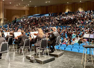 photo of orchestra onstage and kids in audience