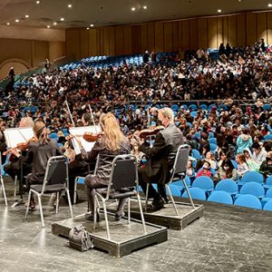 photo of orchestra onstage and kids in audience